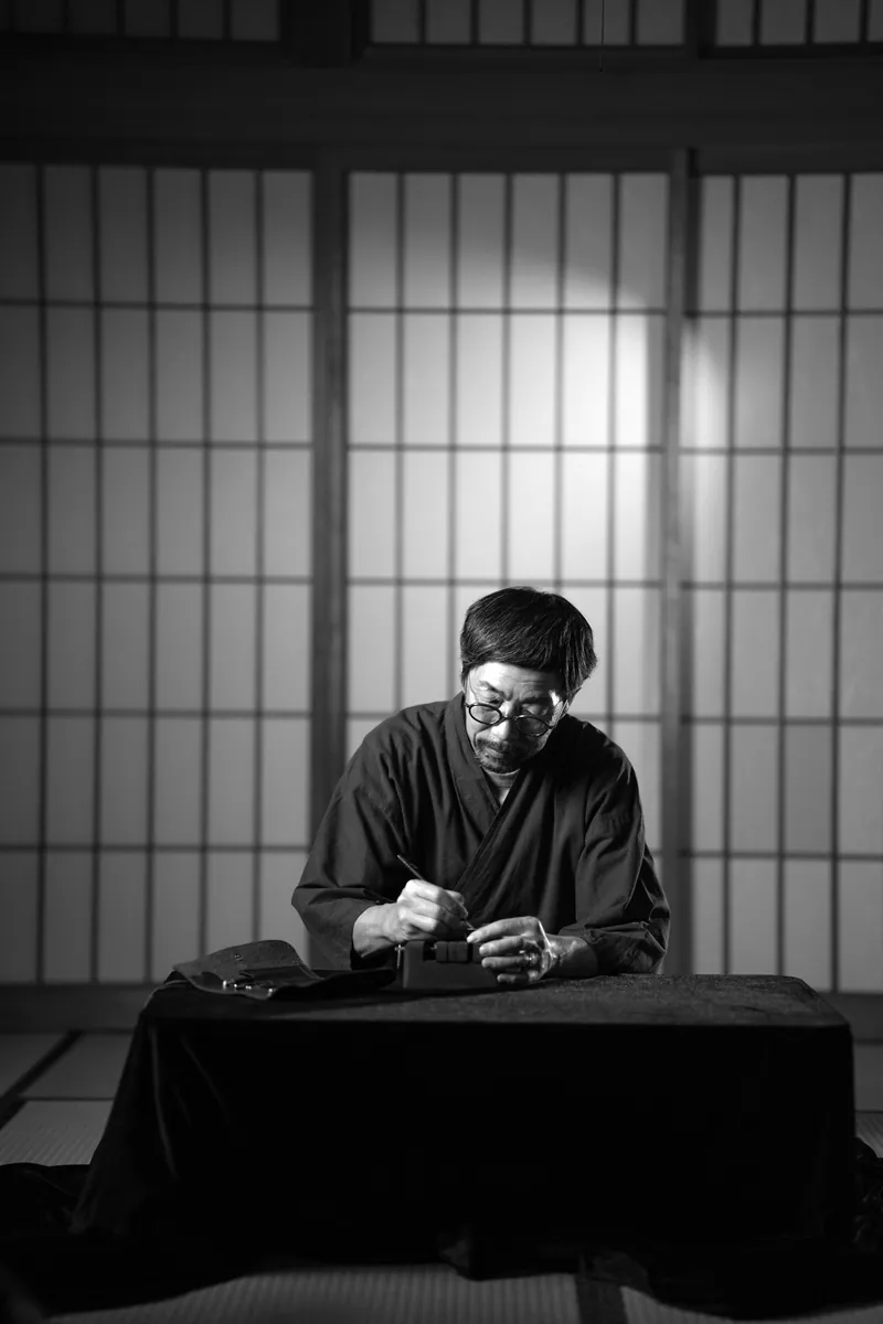 Black-and-white portrait of our craftsman carving at his table